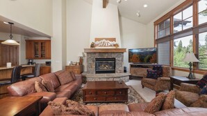 A spacious living room with a stone fireplace, leather sofas, and a large window offering a view of trees.