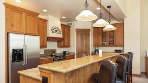 A kitchen with wooden cabinets, stainless steel appliances, a granite countertop, and bar seating.
