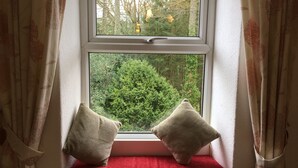 Janela com vista para uma floresta, um banco vermelho e duas almofadas.