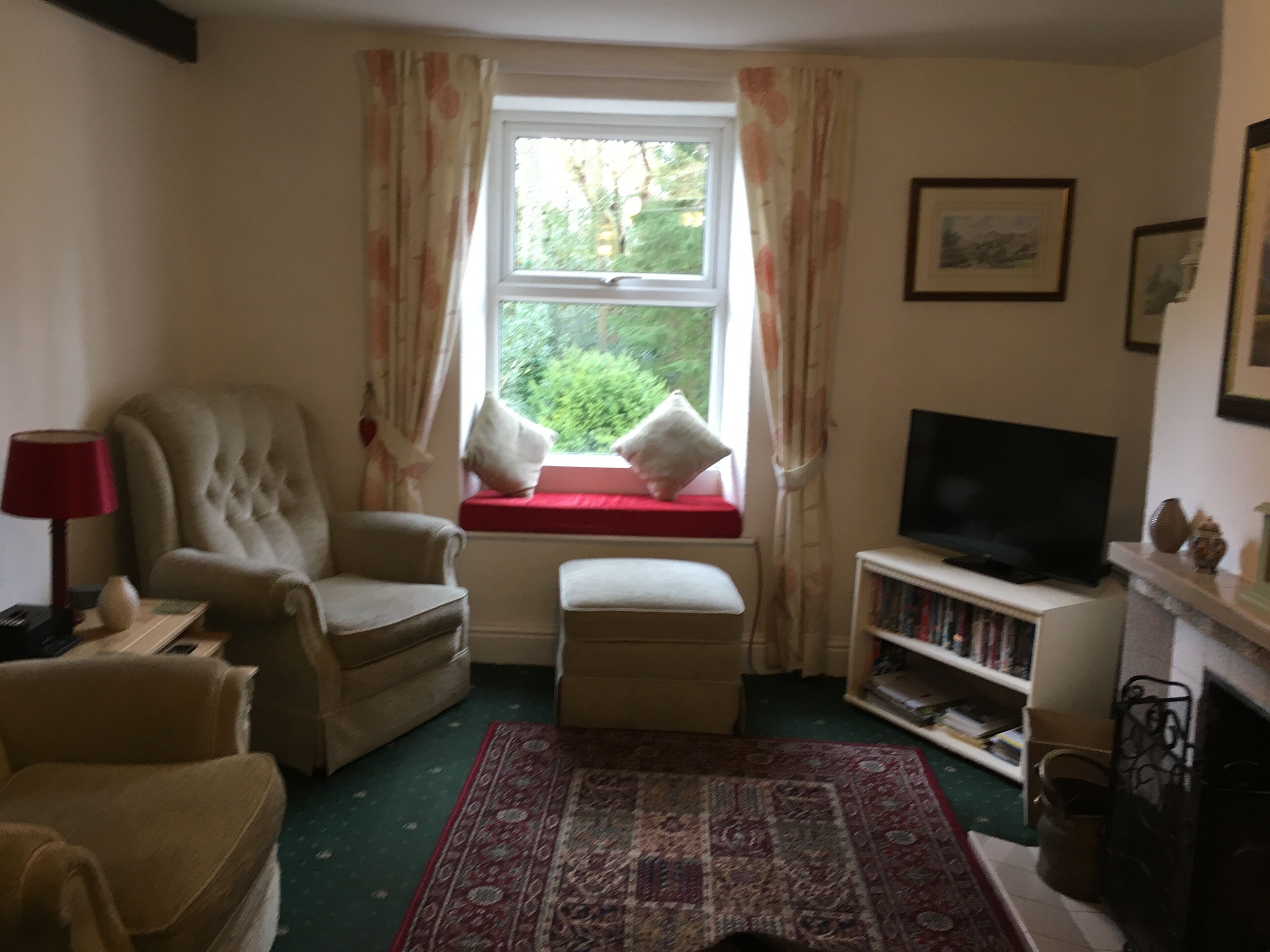 A living room with a large armchair, a sofa, a television, a bookshelf, and a window with curtains.