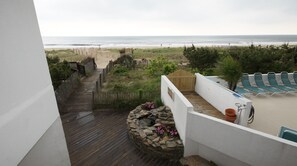 Un balcon donnant sur la plage, avec vue sur l’océan, une terrasse en bois et un espace salon agrémenté d’un bac à fleurs en pierre.