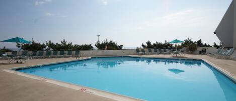 A swimming pool with lounge chairs and umbrellas, surrounded by trees and a clear sky.