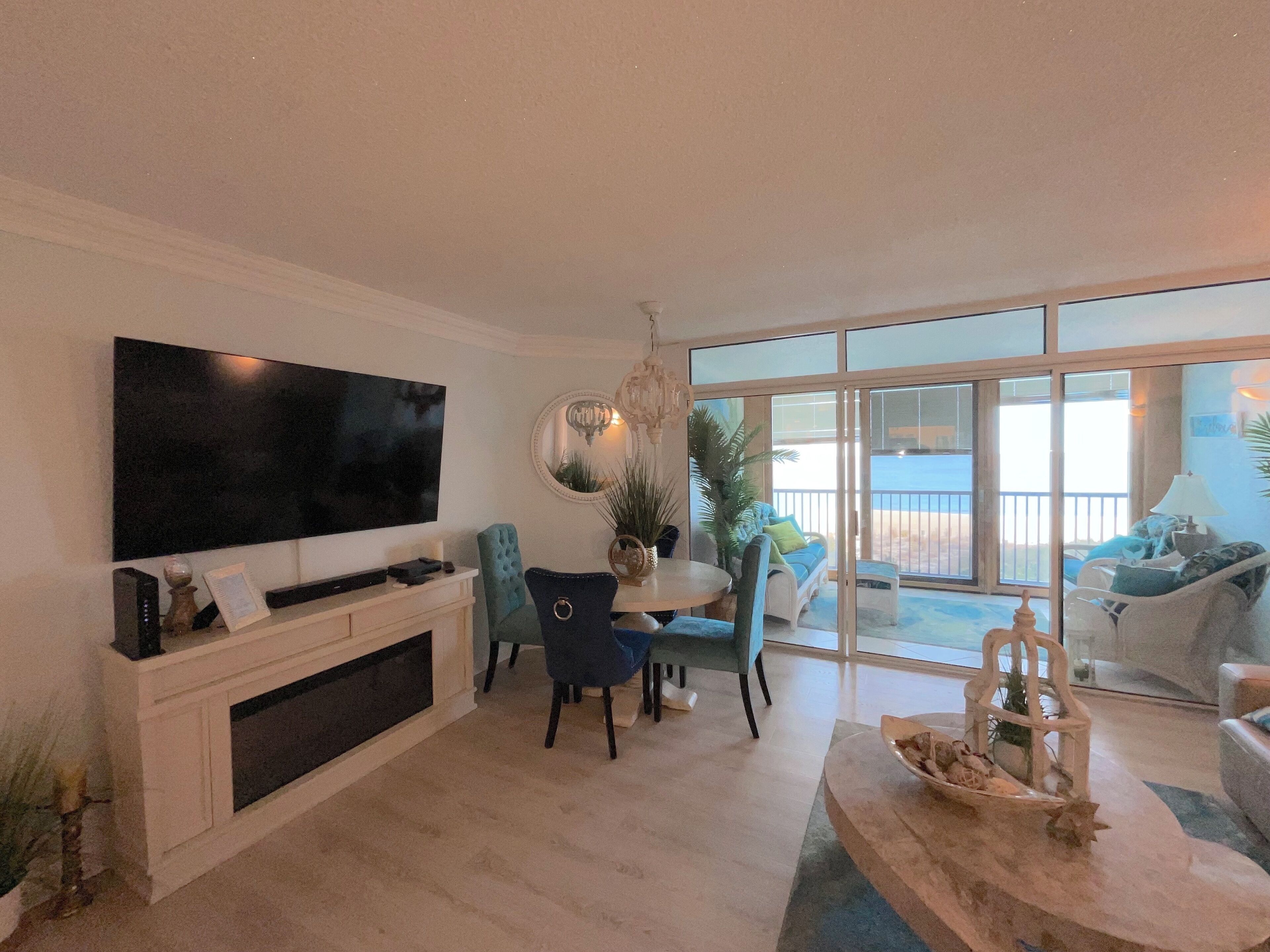 Una sala de estar moderna con un televisor de pantalla plana, un comedor con mesa y sillas, y un balcón con vistas al mar.