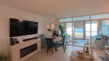 Una sala de estar moderna con un televisor de pantalla plana, un comedor con mesa y sillas, y un balcón con vistas al mar.
