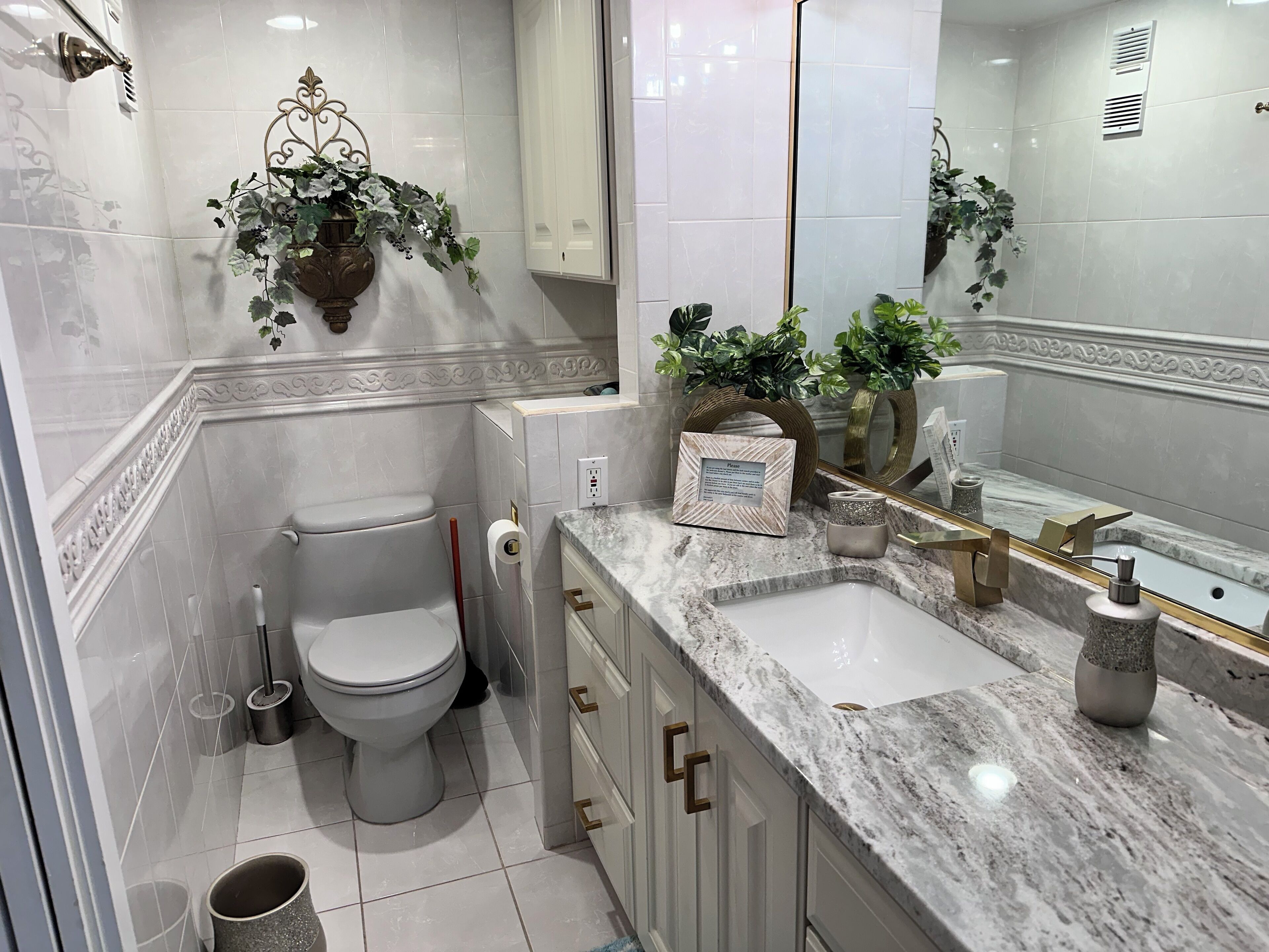 A modern bathroom with a marble sink, a toilet, and decorative plants.