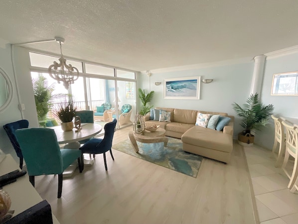 A spacious living room with a large sofa, a dining table with chairs, and several potted plants. - Delightful Escape, Oceanfront 2BDR , Awesome Views, Pool, Clean! (Ocean City)