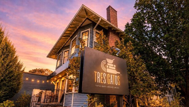 A two-story building with a sign for 'Tres Gatos' featuring a bar, books, and music. - Sunny 4 Bed/2 Bath Victorian Oasis in the City! (Boston)