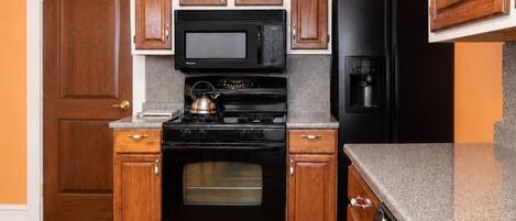A kitchen with wooden cabinets, a black stove, a microwave, and a refrigerator.