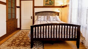 A bedroom with a wooden bed, a patterned rug, a door, and a painting on the wall. - Sunny 4 Bed/2 Bath Victorian Oasis in the City! (Boston)