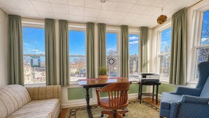 A room with a sofa, a dining table with chairs, a printer, and large windows with curtains. - Sunny 4 Bed/2 Bath Victorian Oasis in the City! (Boston)