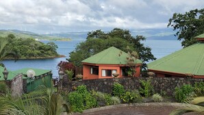 A coastal property with a stone wall, a green-roofed building, and a view of the sea and distant hills.