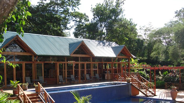 A pool area with a wooden deck, lounge chairs, and a covered seating area.
