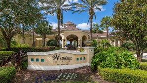 A landscaped entrance with a sign for Windsor Hills Clubhouse, surrounded by palm trees and well-maintained hedges.