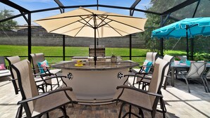 A covered outdoor patio with a grill, seating area, and umbrellas.