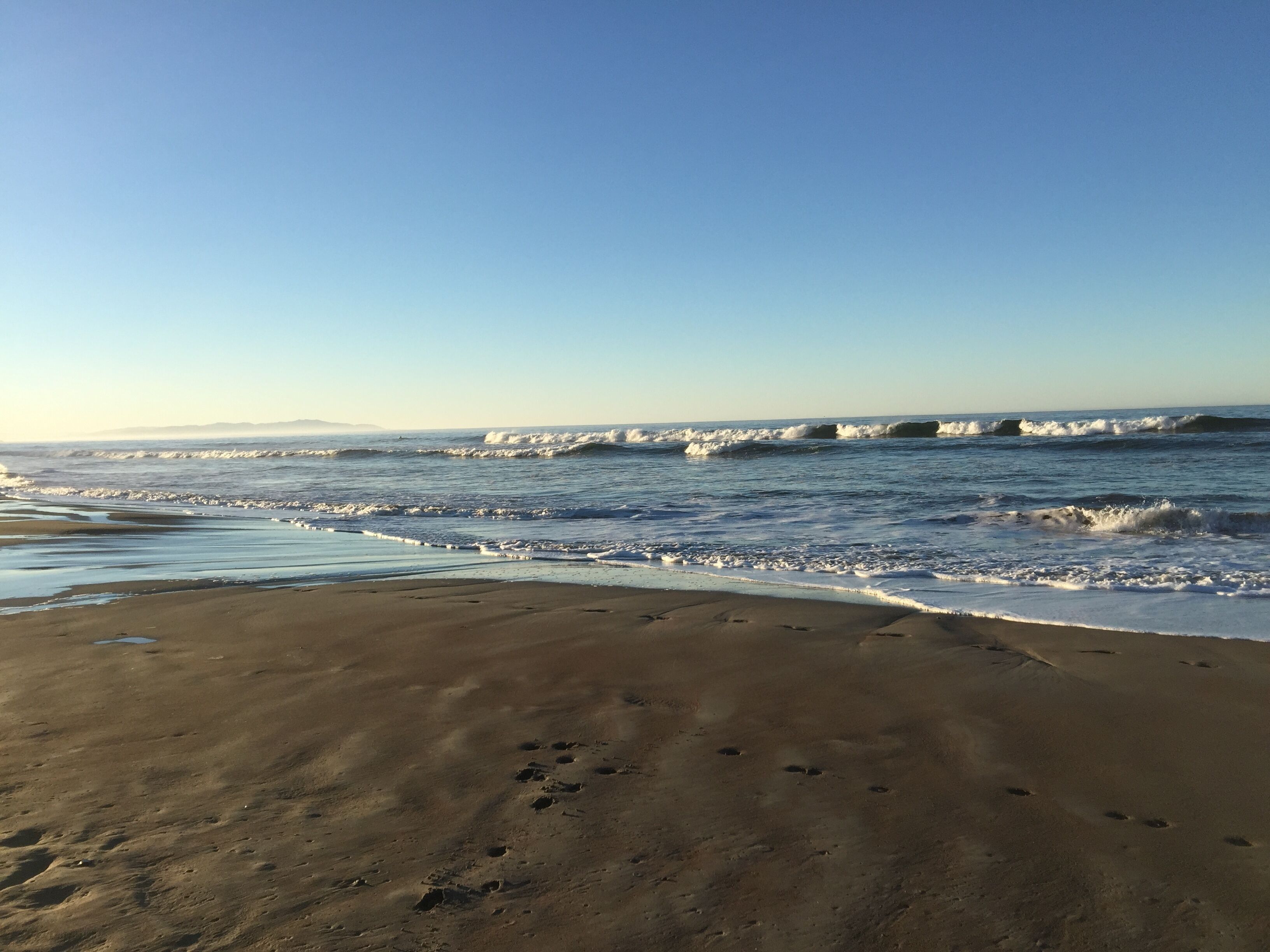 A beach with waves and footprints in the sand.