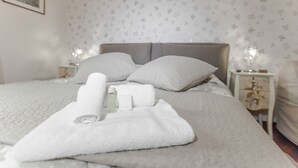 A neatly made bed with white linens, a rolled towel, and a bottle of lotion on the side.
