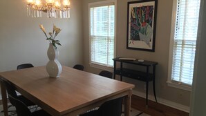 Un comedor con una mesa de madera, sillas negras, un jarrón con flores, una araña y un cuadro en la pared.