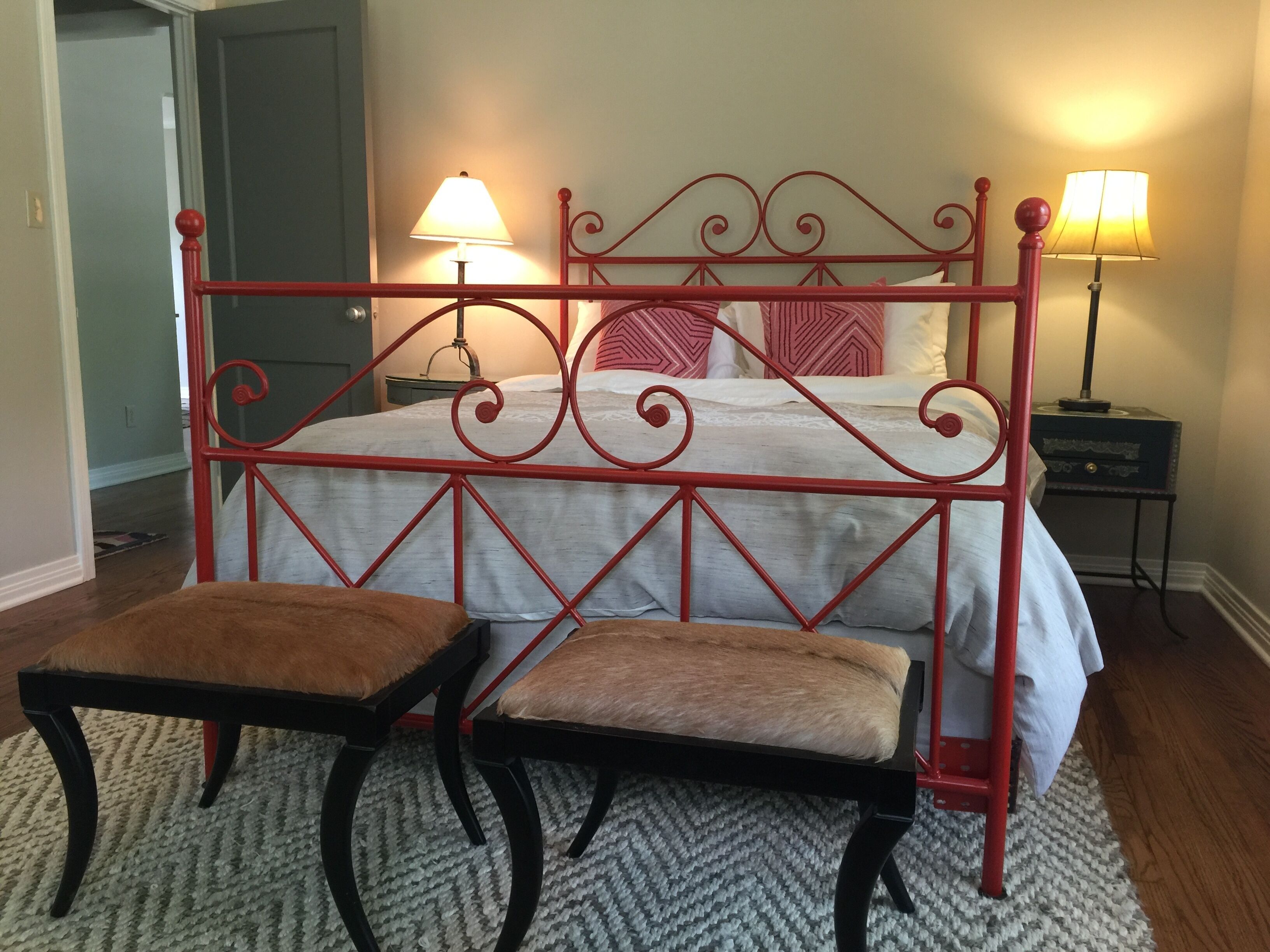 A bed with a red metal frame, two bedside tables, and two chairs.