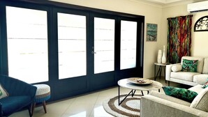 A living room with a large sliding glass door, a white sofa, a blue armchair, and a round coffee table. - Piece of Paradise... Eagle Beach Villa with Private Pool;  Great Location! (Aruba)