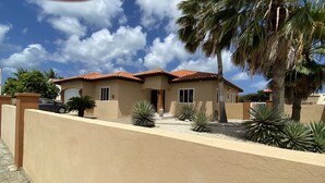 A two-story house with a tiled roof, beige walls, and a small front yard with palm trees and agave plants. - Piece of Paradise... Eagle Beach Villa with Private Pool;  Great Location! (Aruba)