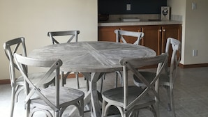 A dining area with a round wooden table and six chairs, a hanging light fixture, wooden cabinets, and a tiled floor. - Wild Rose Ranch Guest Cabin (Baraboo)
