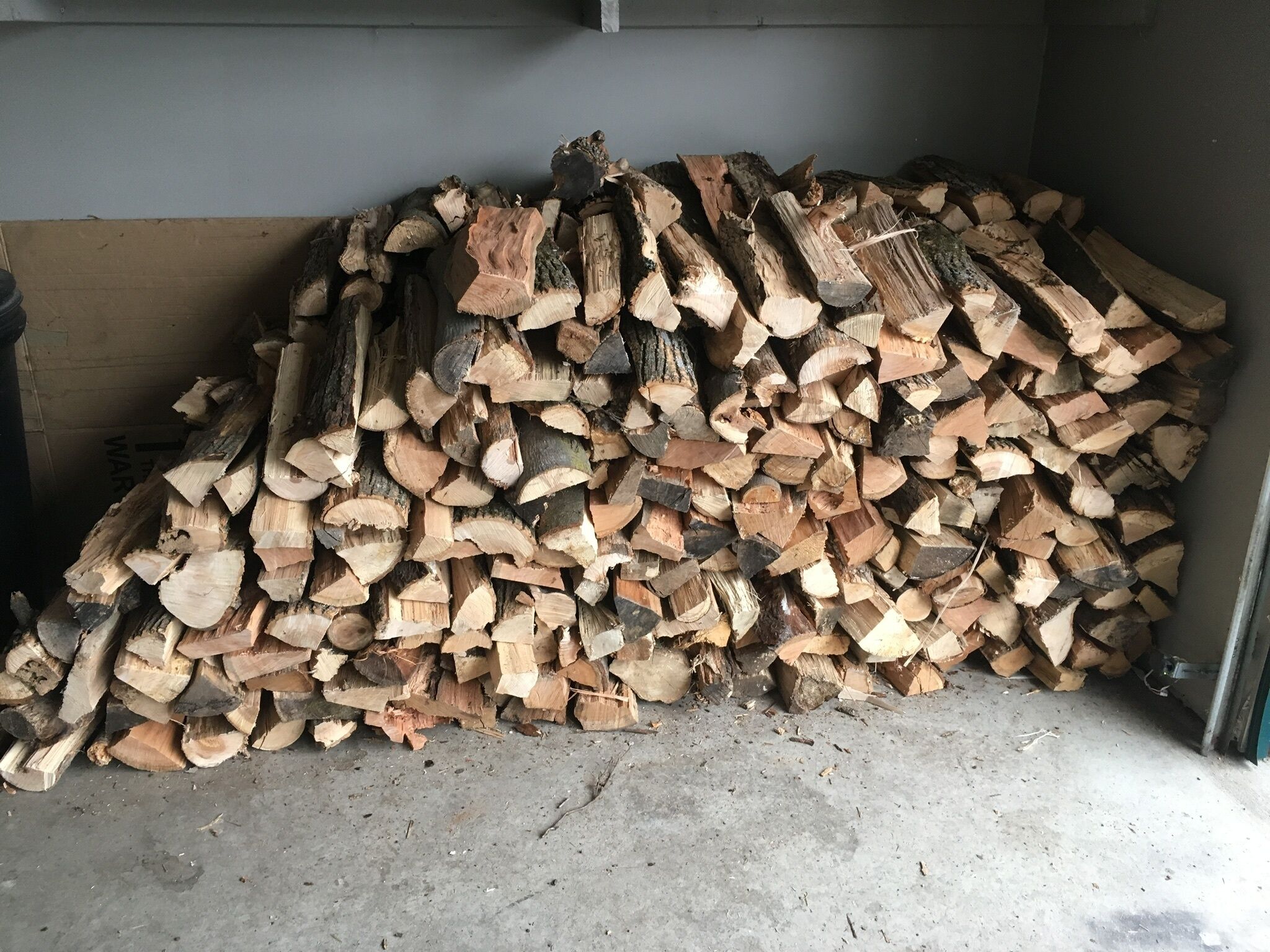 A stack of firewood against a wall in a room with a concrete floor.
