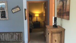 A hallway with a wooden bench, a cabinet, a bed, and a painting on the wall. - Wild Rose Ranch Guest Cabin (Baraboo)