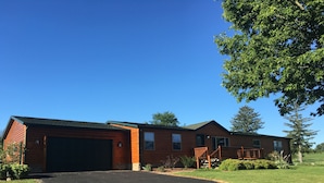 A two-story log cabin with a garage, a covered porch, and a well-maintained lawn. - Wild Rose Ranch Guest Cabin (Baraboo)