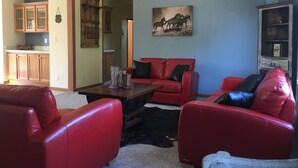 A living room with red leather sofas, a coffee table, and a painting on the wall. - Wild Rose Ranch Guest Cabin (Baraboo)