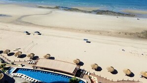 Un complexe hôtelier en bord de mer doté d’une piscine, de parasols et offrant une vue dégagée sur l’océan.