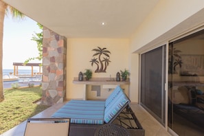 A patio with a lounge chair, a stone wall, a palm tree mural, and a view of the ocean.