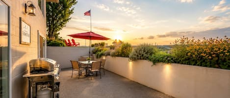 An outdoor patio with a grill, chairs, and a red umbrella.