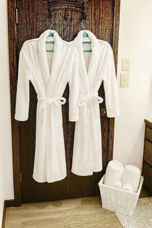 Deux robes blanches suspendues à une porte, un panier en osier rempli de serviettes et un plancher en bois.
