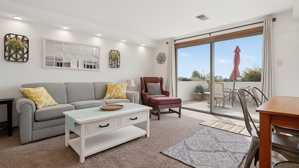 Una sala moderna con un sofá gris, una mesa de centro blanca y un sillón rojo. Hay una puerta corrediza de vidrio que da a un patio al aire libre.