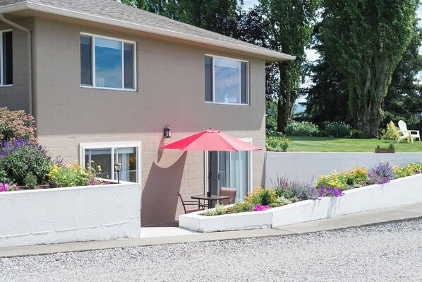 A two-story house with a patio area featuring a red umbrella, a small table, and chairs.