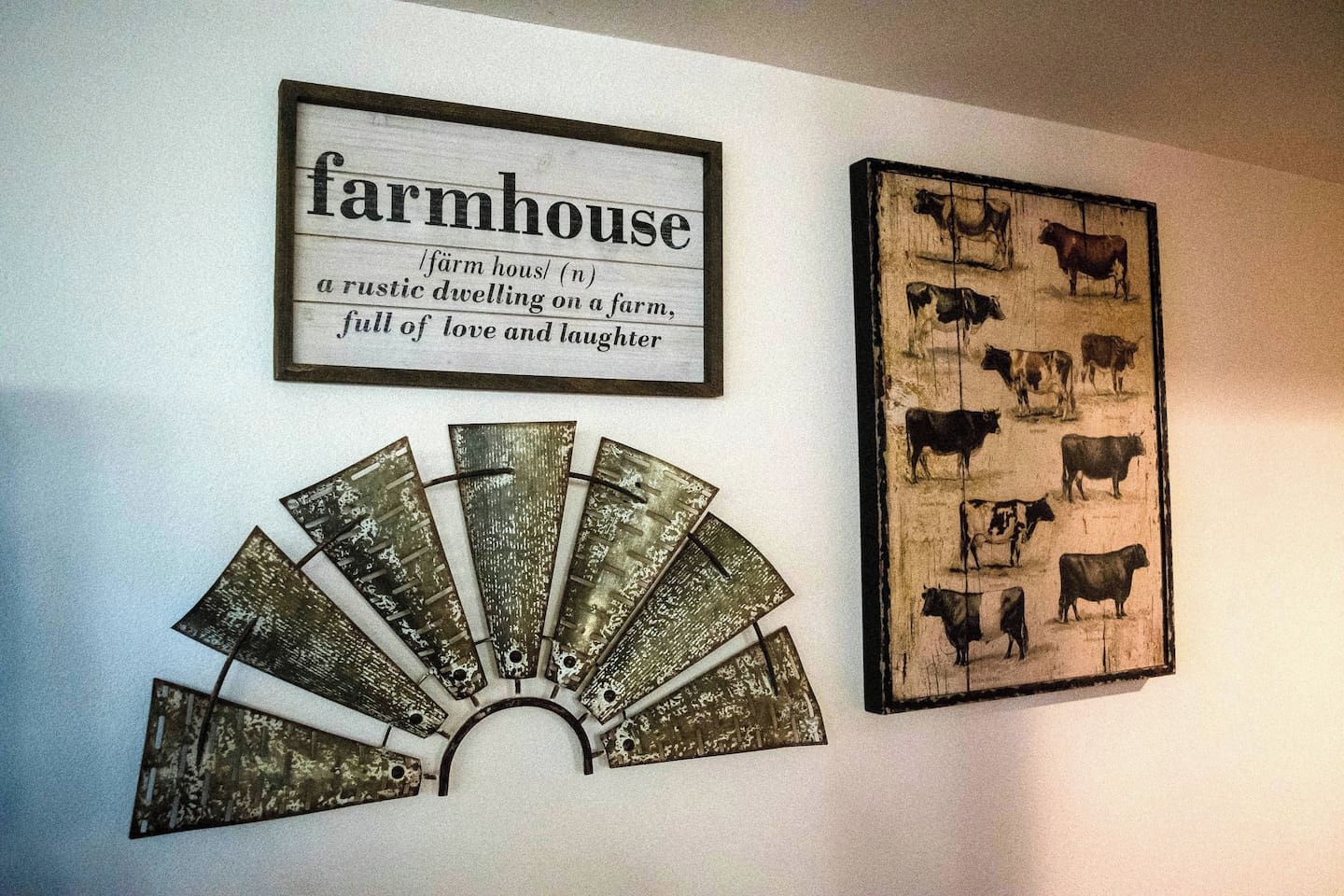 Een muur met een lijst waarin 'farmhouse' gedefinieerd staat, een rustiek houten bord en een illustratie van koeien in een lijst.