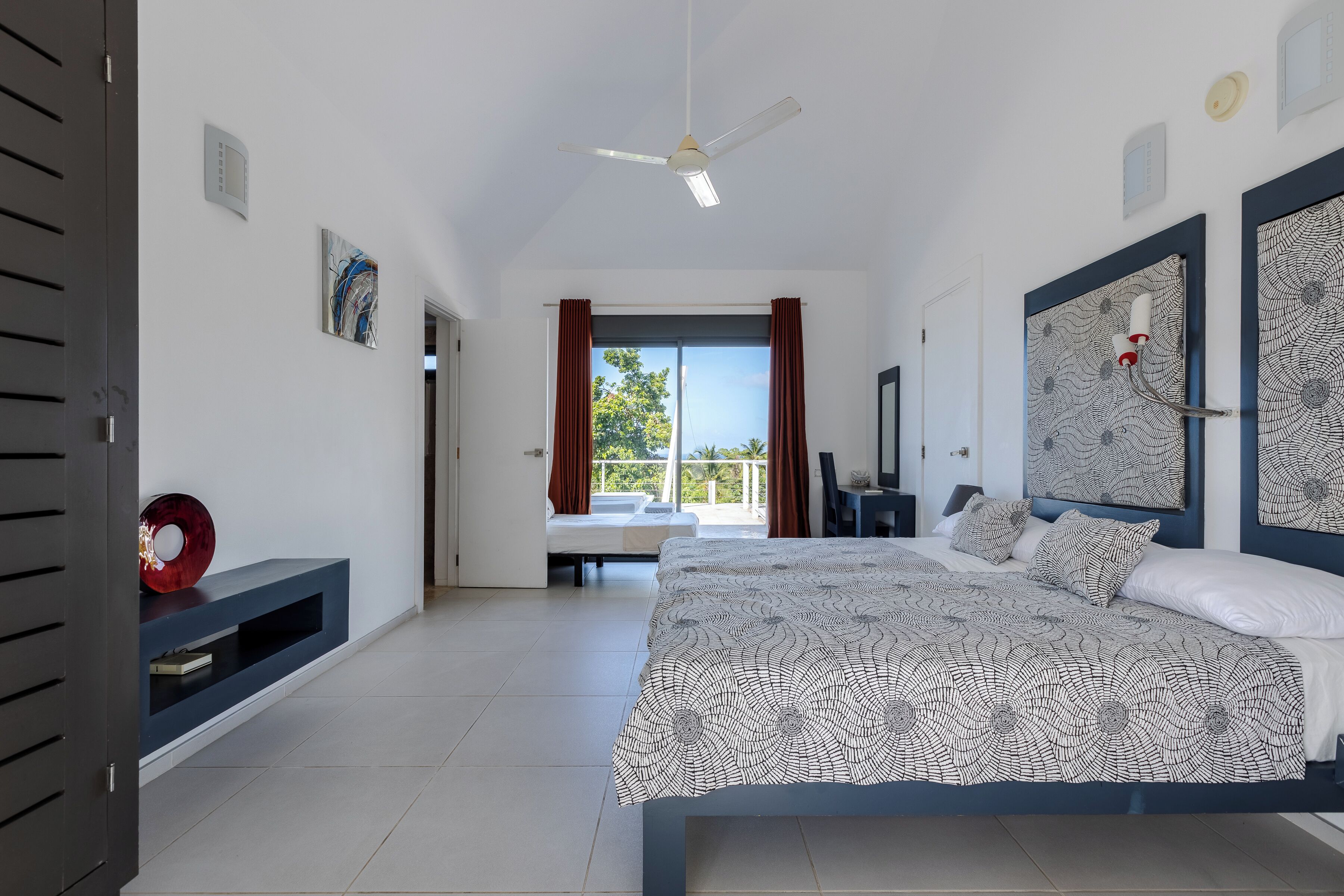 Ein modernes Schlafzimmer mit einem großen Bett, einem Deckenventilator und Blick ins Freie.