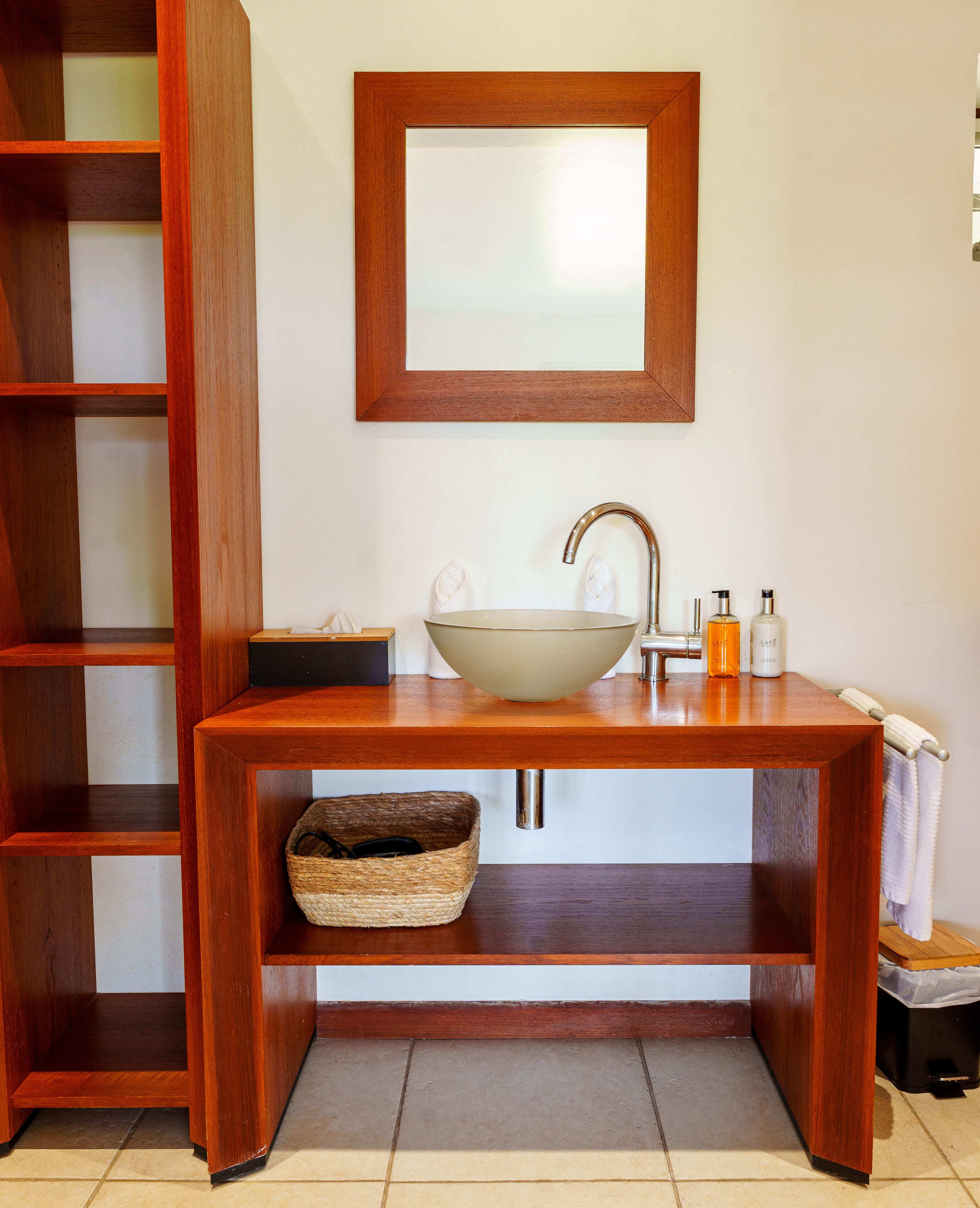 Un baño con tocador de madera, un espejo grande, un lavabo sobre encimera y un perchero para toallas.
