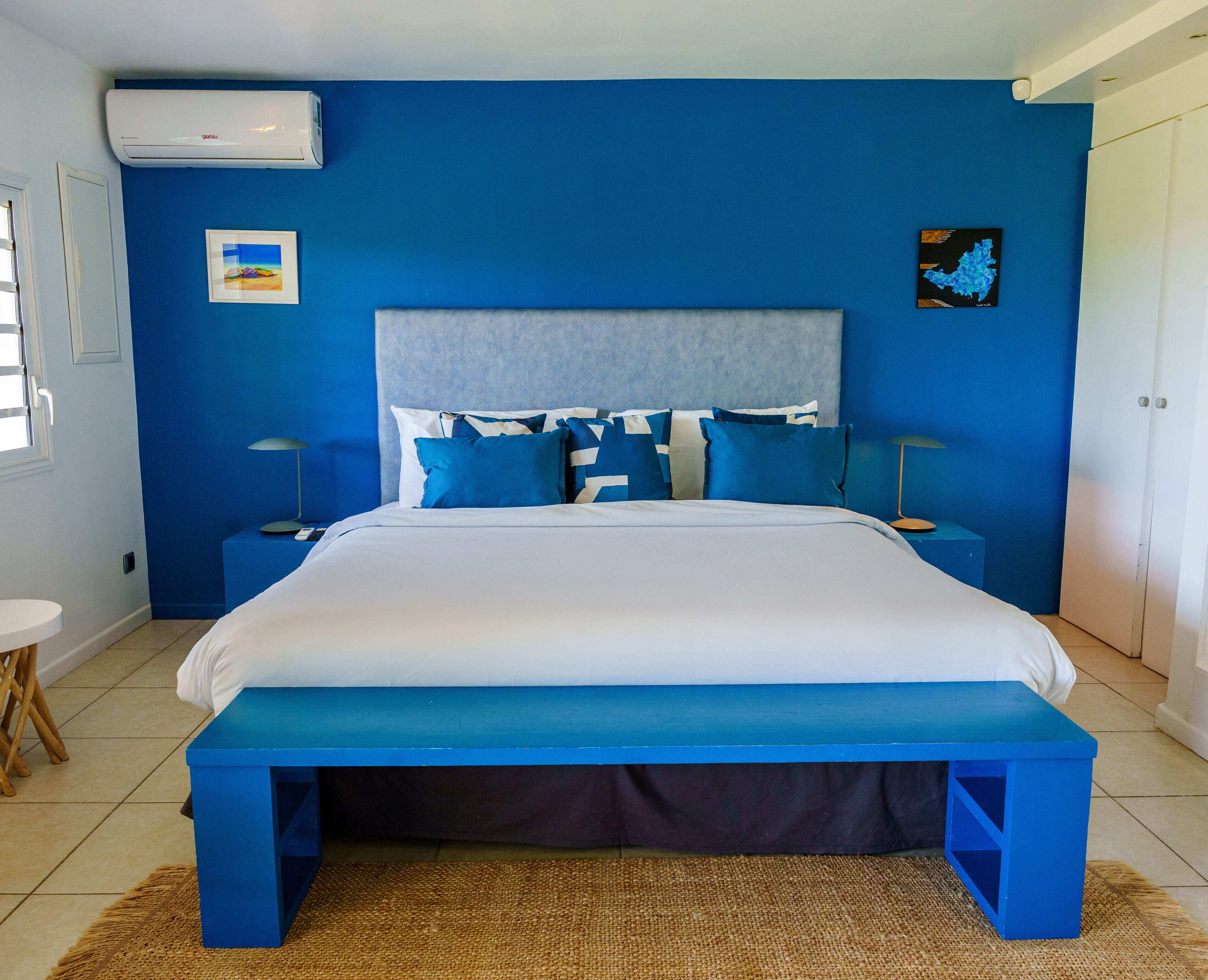 A bedroom with a bed, a headboard, bedside tables, a nightstand, a wall-mounted air conditioner, and a door.