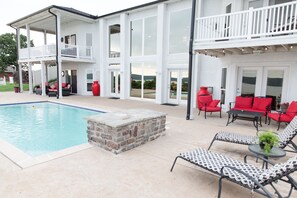 A two-story house with a swimming pool, outdoor seating, and a stone fire pit.