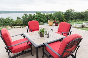 A patio with a table and four red chairs, surrounded by potted plants and a view of a lake.