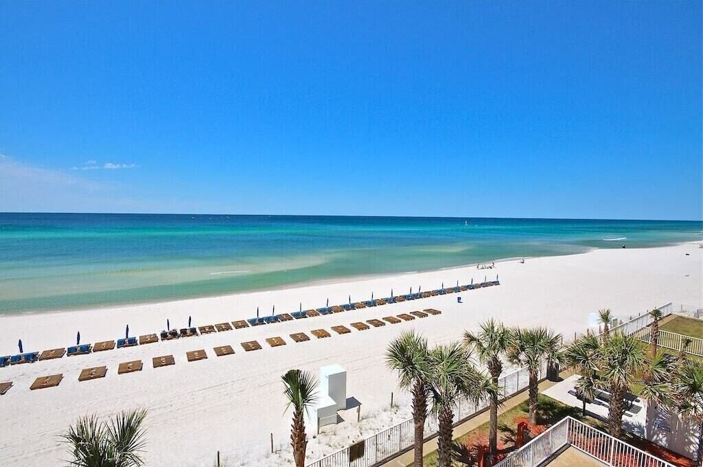 A beach with rows of sun loungers and palm trees, leading to the ocean.