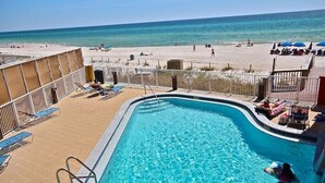 Un espace piscine avec vue sur la plage, des chaises longues et des parasols.