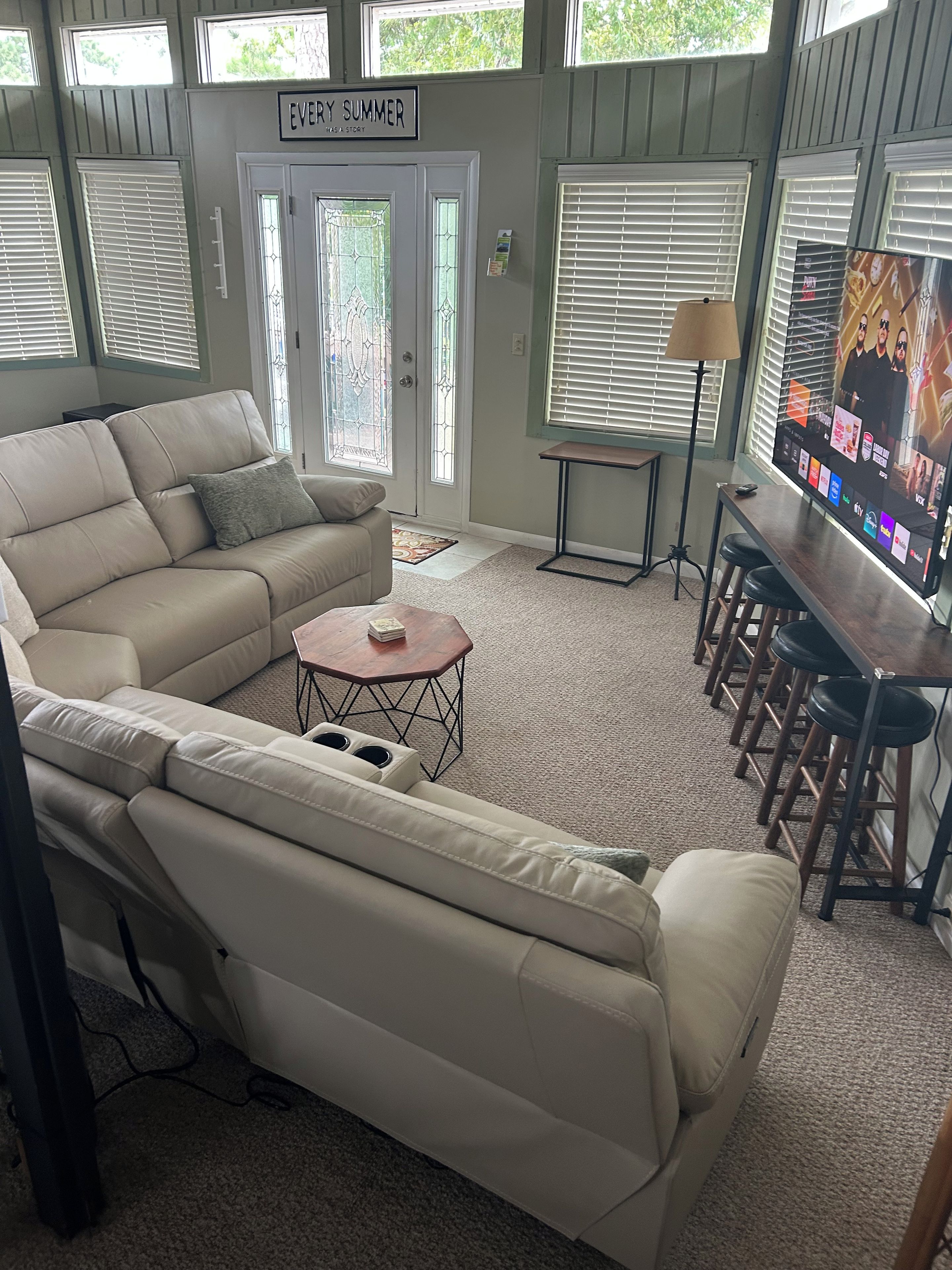 A living room with a beige sectional sofa, a small round coffee table, a TV on a stand, and a bar area with stools.