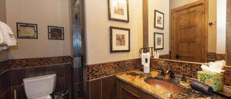 A bathroom with a toilet, sink, and mirror. There are framed pictures on the wall and a towel rack.