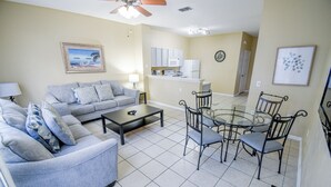 Sala de estar con sofá, mesa de centro y mesa de comedor con sillas. Cuenta con una zona de cocina con armarios y electrodomésticos.