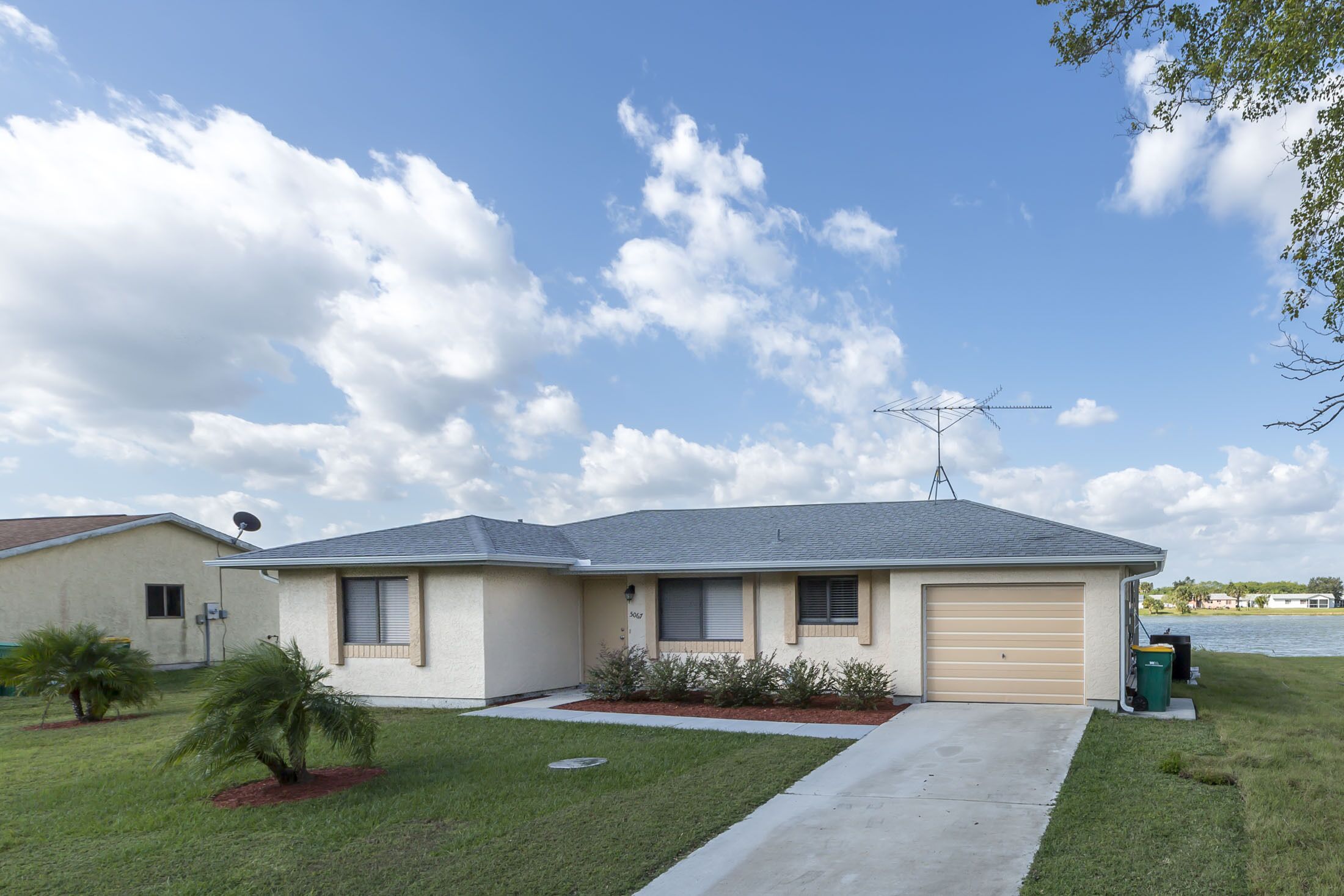 A single-story house with a garage, satellite dish, and a small lawn with a palm tree.