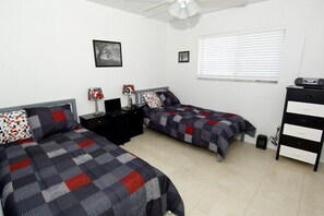 Une chambre avec deux lits, une table de chevet, une commode et un ventilateur de plafond.