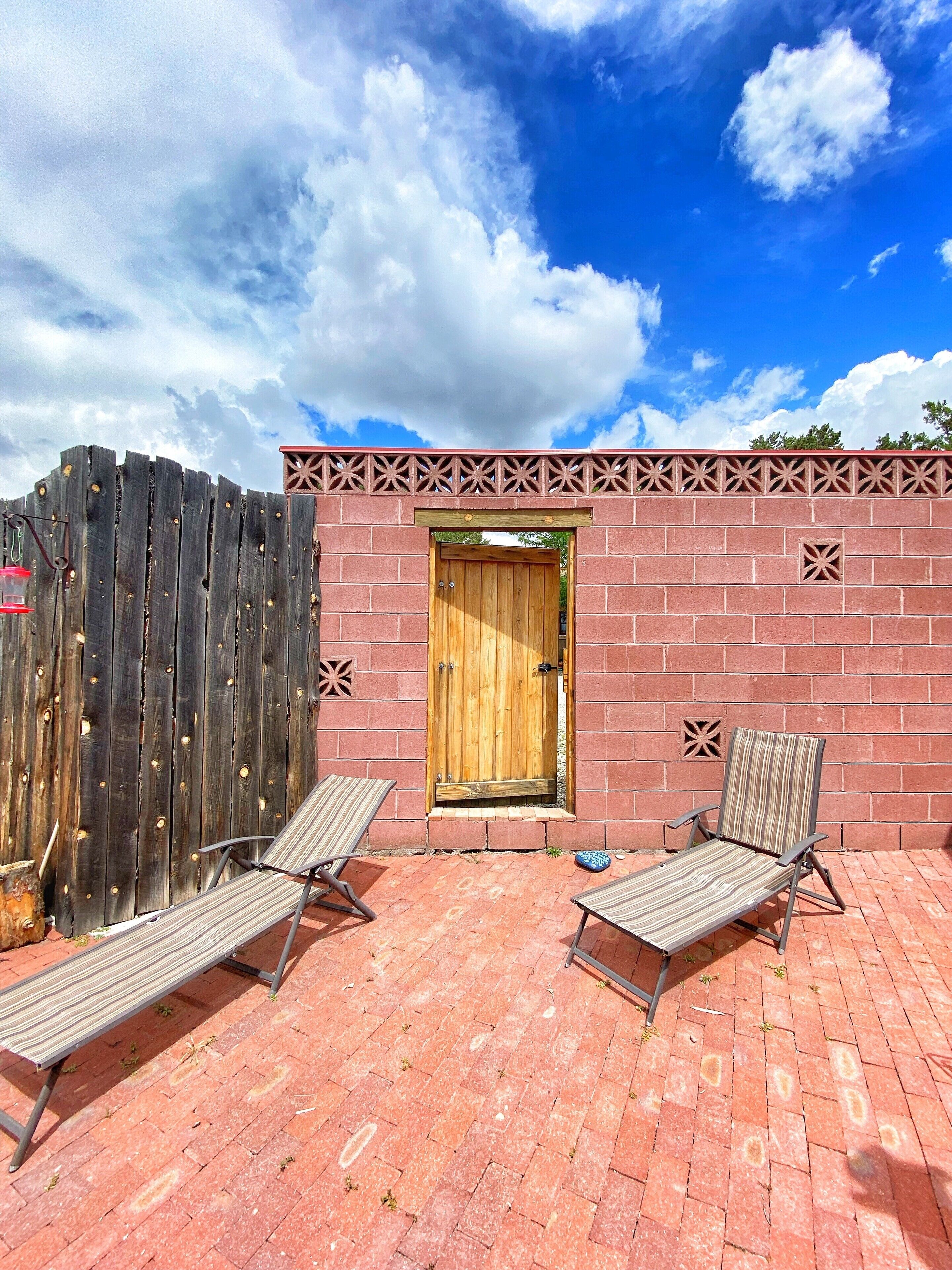 Un patio con dos tumbonas, una puerta de madera y un muro de ladrillo.
