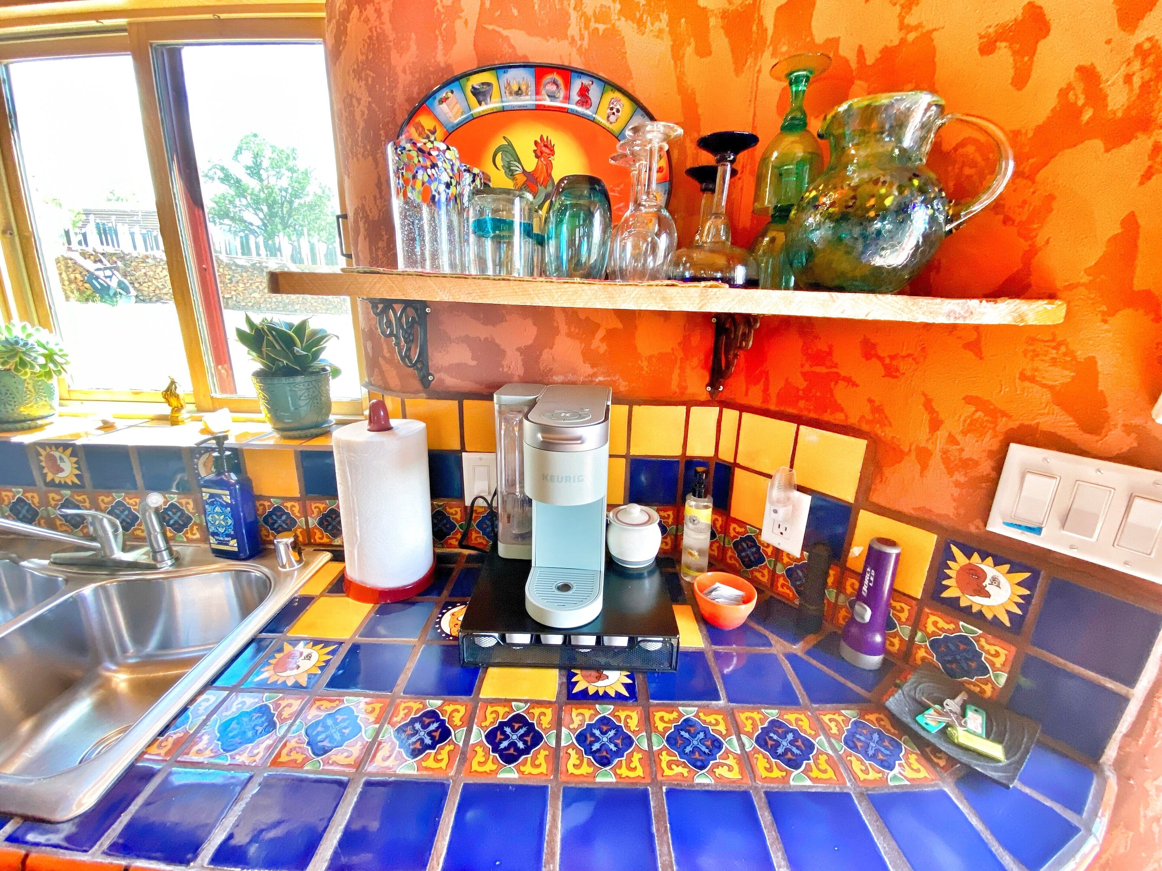 Una cocina con un salpicadero de azulejos coloridos, una cafetera y varios utensilios de cocina sobre la encimera.